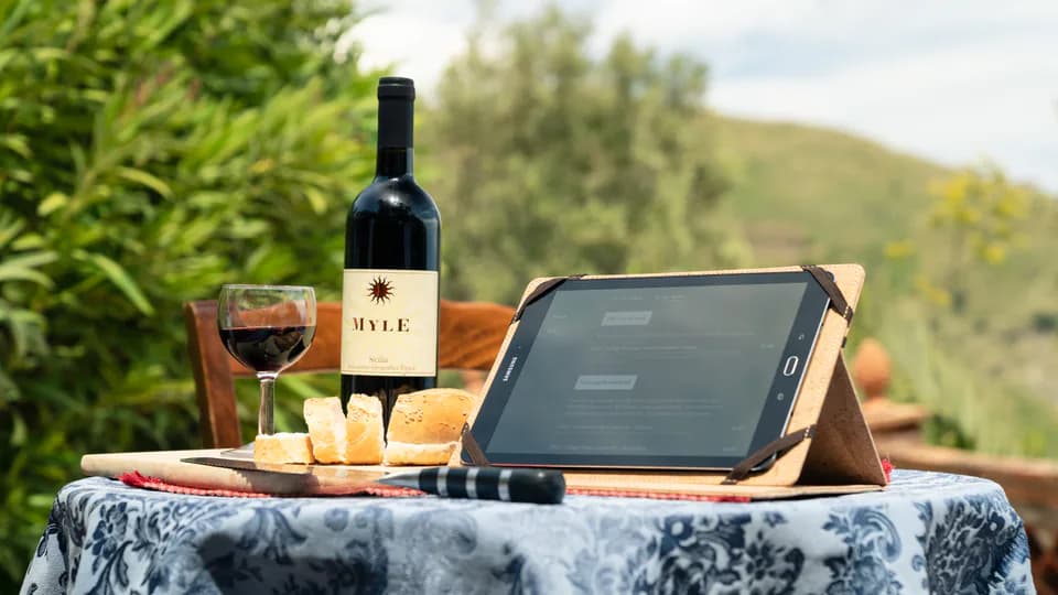Een fles rode wijn, een glas en een tablet op een tafel in een Siciliaanse tuin.